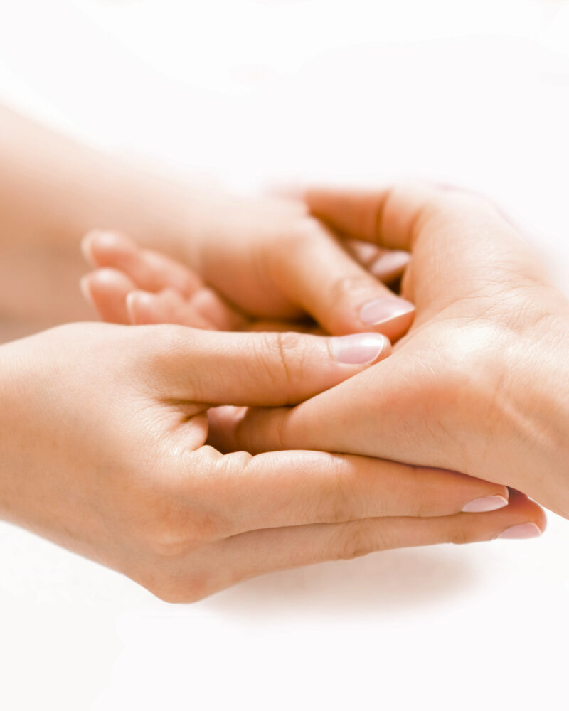 A white upturned hand is massaged by two other white hands coming from the opposite direction.