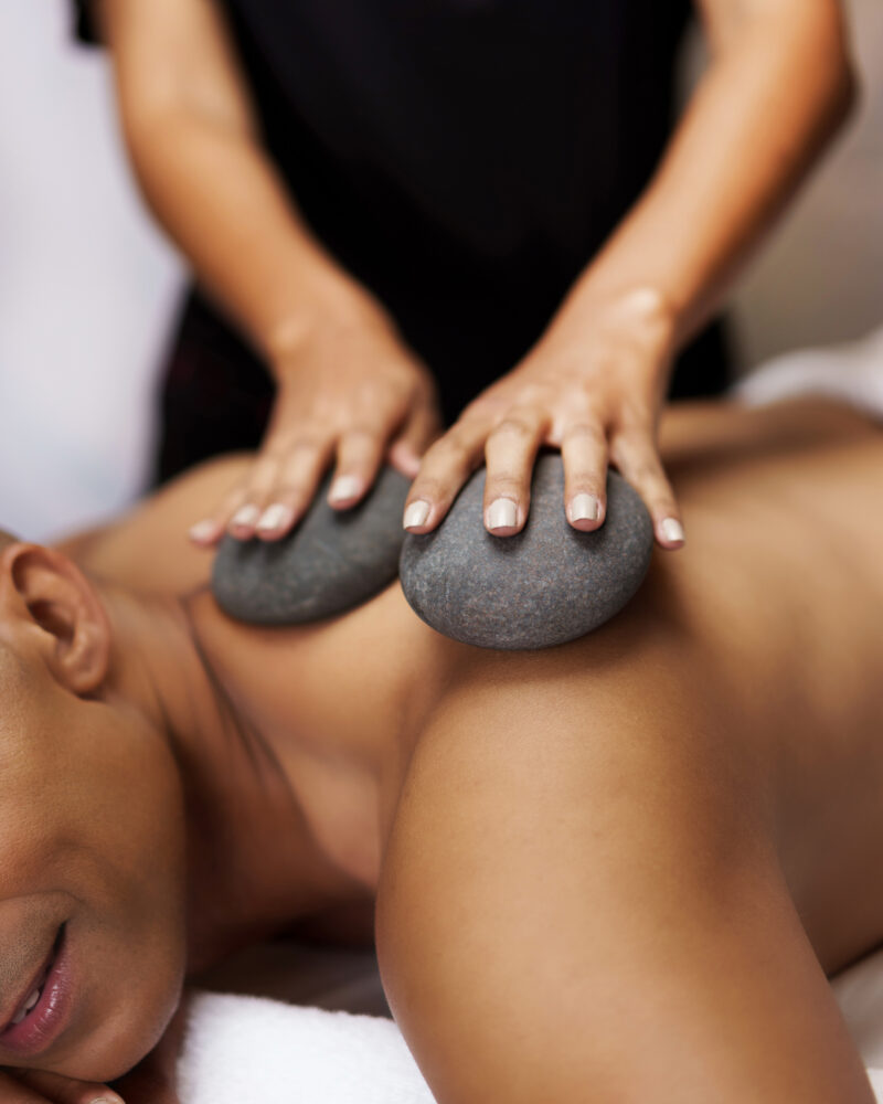 A masseuse's hands placing gray stones onto a man's shoulder.