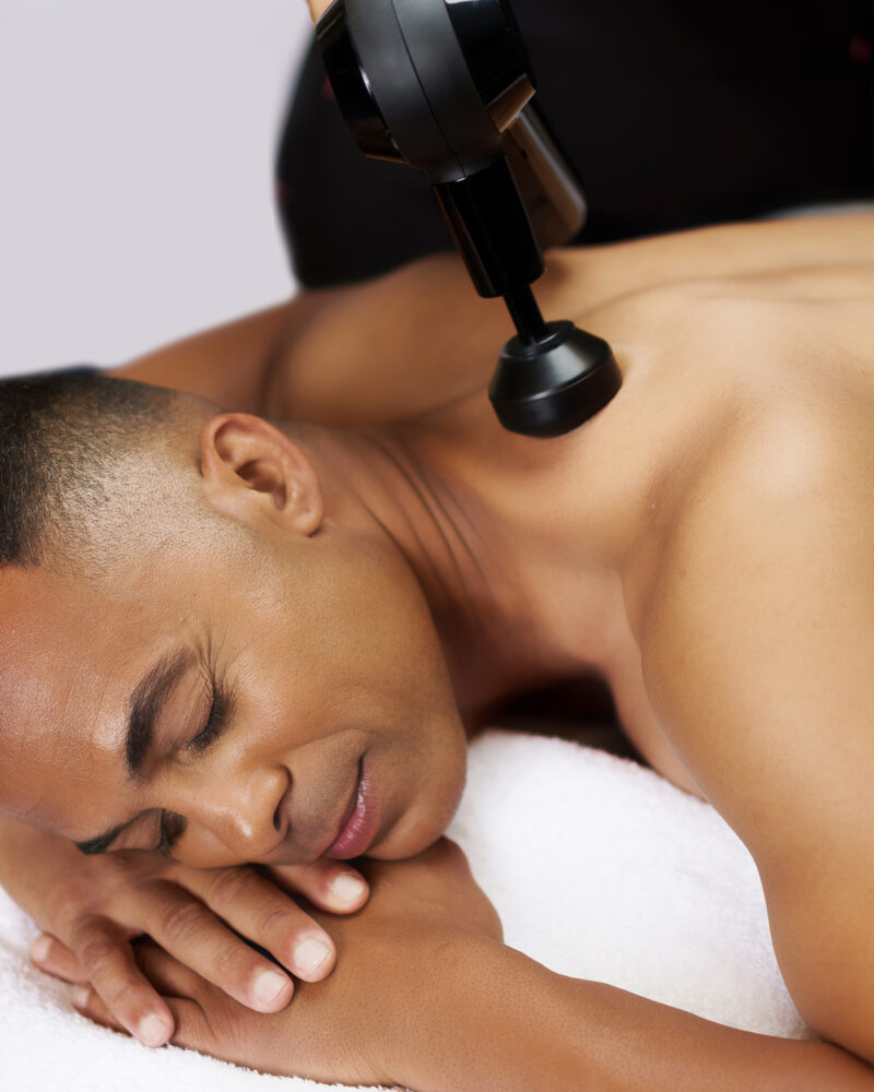 A black man receiving massage therapy from an electronic device.