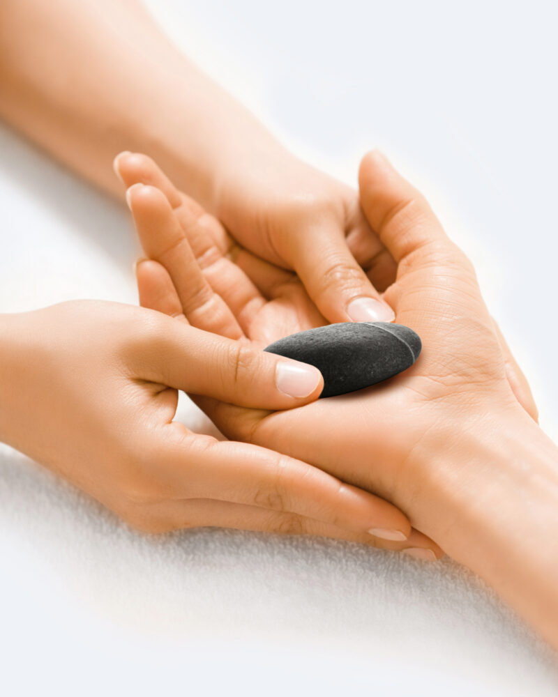 A masseuse's hands placing a black stone into a woman's palm.