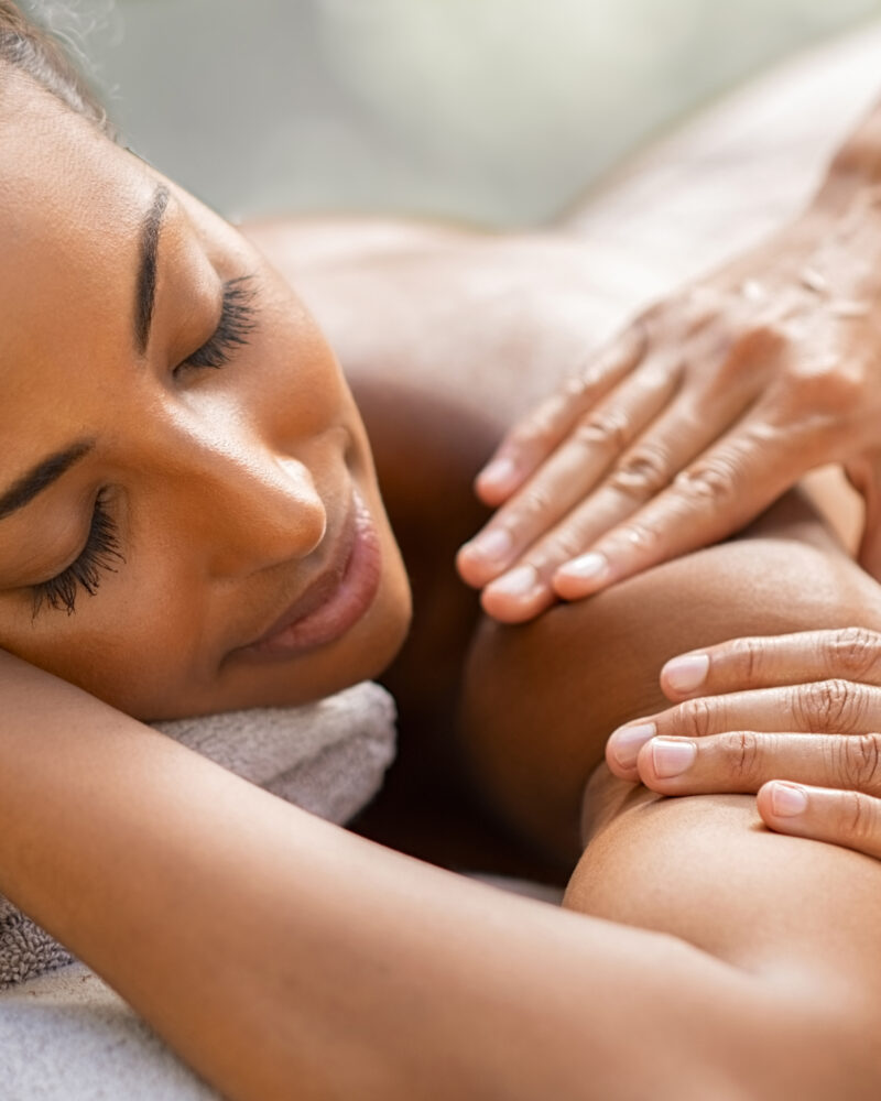 A masseuse's hands massaging the shoulder of a black woman.